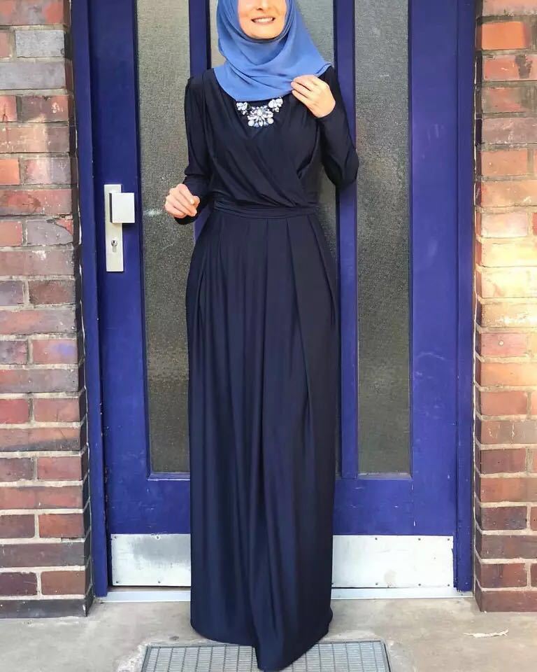 Woman wearing a navy blue maxi dress with a tie waist and embellished neckline, standing in front of a blue door.