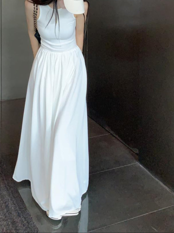 Woman wearing a sleeveless white maxi dress and a cap, standing indoors against a modern backdrop.