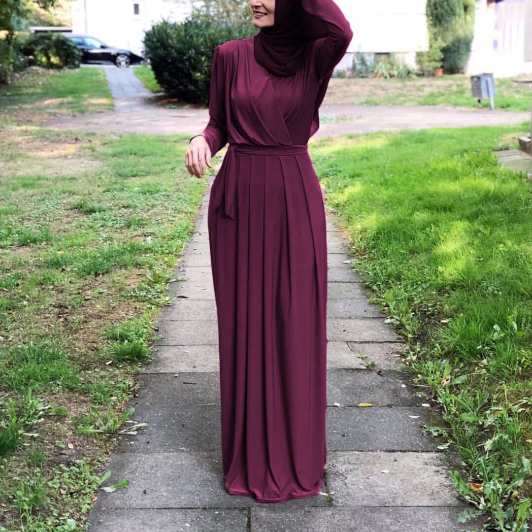 Woman in a burgundy V-neck tie pleated maxi skirt walking on a path surrounded by greenery.
