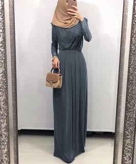 Woman in a long, gray pleated maxi dress with a hijab and a stylish handbag, posing in front of a mirror.