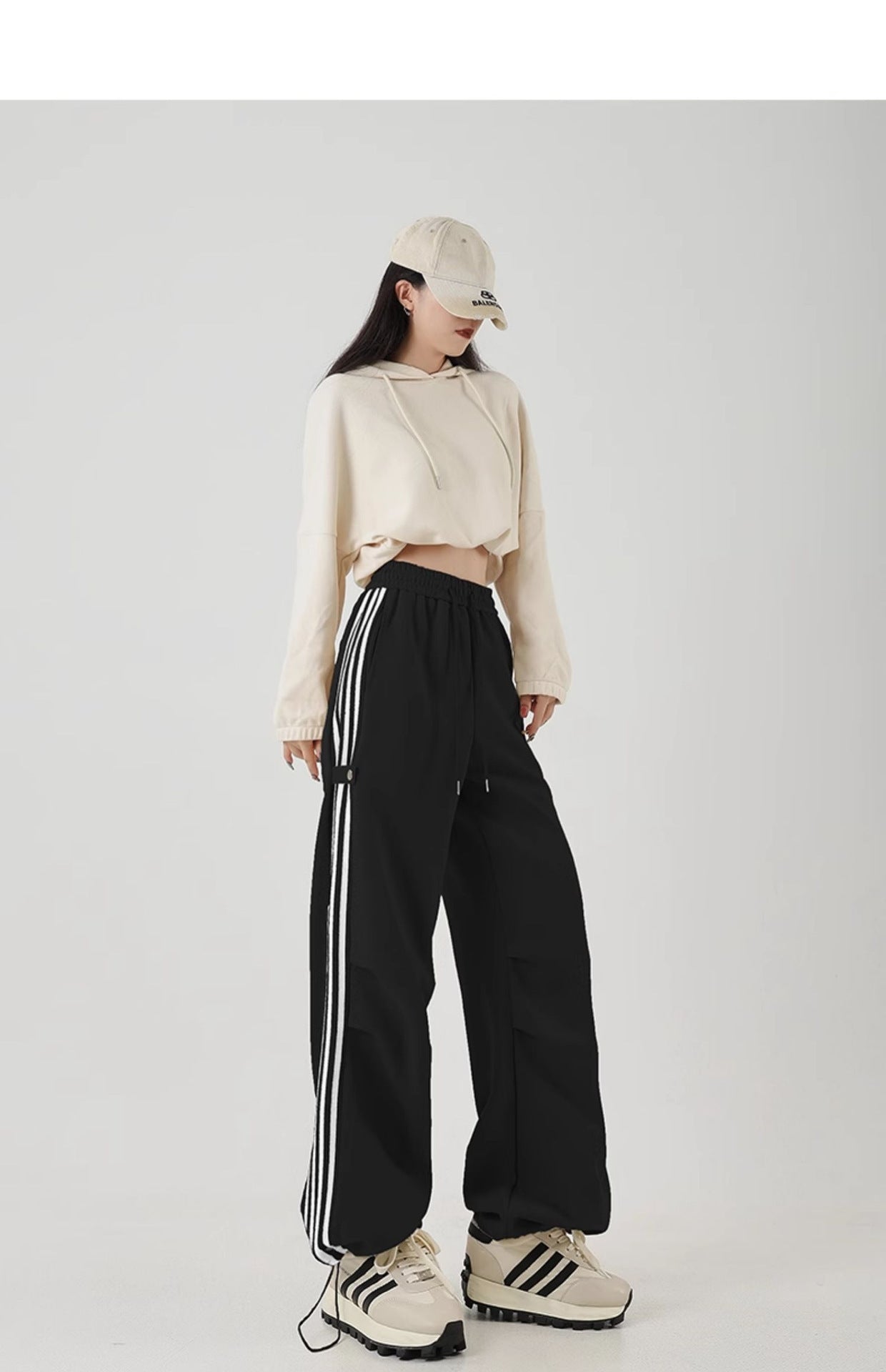 Model wearing wide-leg black cotton sweatpants with white stripes, paired with a cropped hoodie and cap.